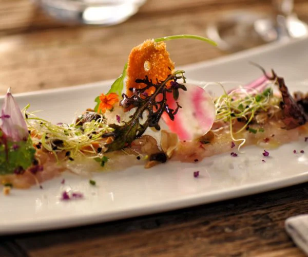 Table de trois restaurants Bordeaux, assiette gastronomique de poisson mariné avec fleurs, radis rose tranché et herbes fines, dressage créatif sur porcelaine blanche