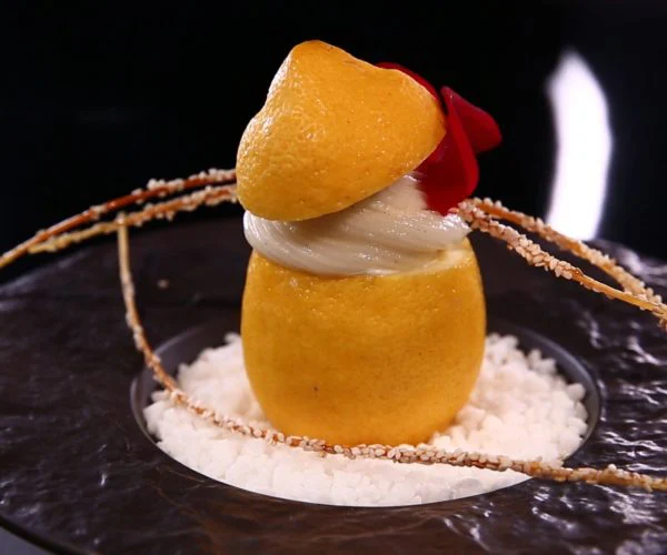Table de trois restaurants Bordeaux, dessert sculpté en forme de citron entier sur lit de riz soufflé, décoré de pétales rouges et de tiges croustillantes, présentation haute couture