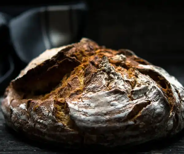 Table de trois restaurants Bordeaux, miche de pain artisanal à la croûte dorée et craquelée, photographiée en clair obscur sur fond sombre