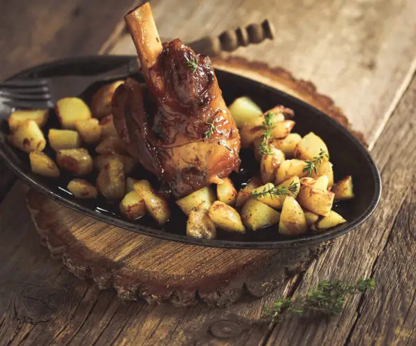 Table de trois restaurants Bordeaux, souris d'agneau fondante aux jus de cuisson avec pommes de terre sautées au thym, servie en cocotte noire sur support en écorce